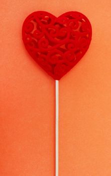 Valentine's Day concept. Copy space. Decorative red gift heart on a stick on an orange background.