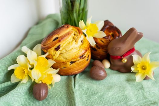 Homemade Easter traditional pastries lie on a green napkin along with daffodil flowers, rabbit, chocolate eggs. Easter baking and decoration