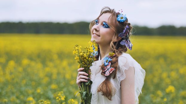 A young girl poses in a rapeseed field with a beautiful hairdo of flowers and butterflies