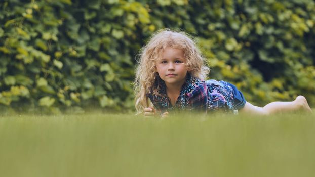 A little curly-haired girl lies on the grass in the garden