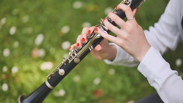 A girl plays the clarinet in the summer in the park. Close-up of her hands