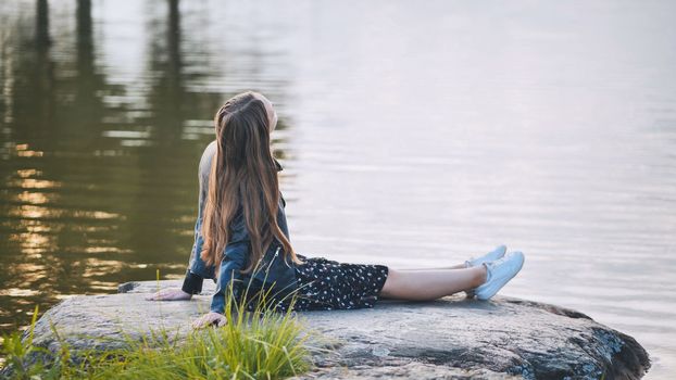 A girl sits by the lake on a rock