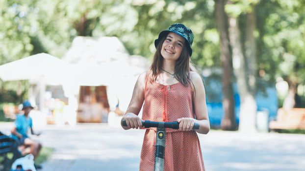 Portrait of a girl on an electric scooter posing in a park in the summer