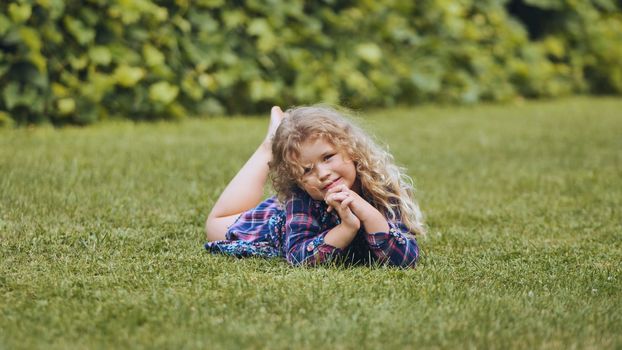 A little curly-haired girl lies on the grass in the garden