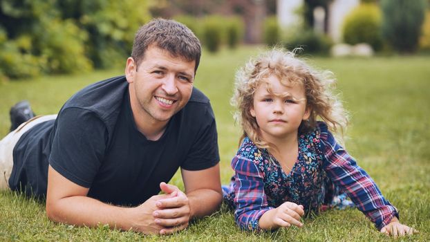 A father kisses his young daughter in the garden while lying on the grass