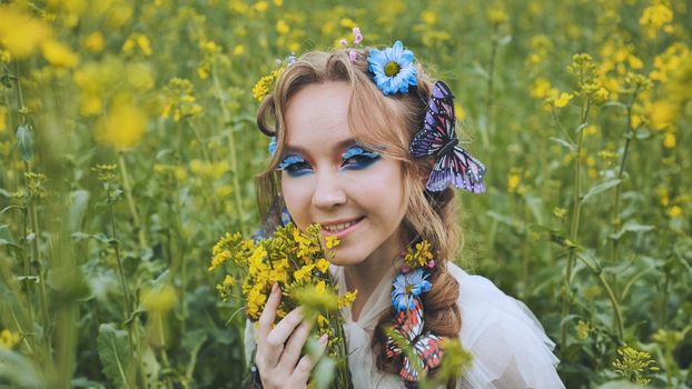 A young girl poses in a rapeseed field with a beautiful hairdo of flowers and butterflies