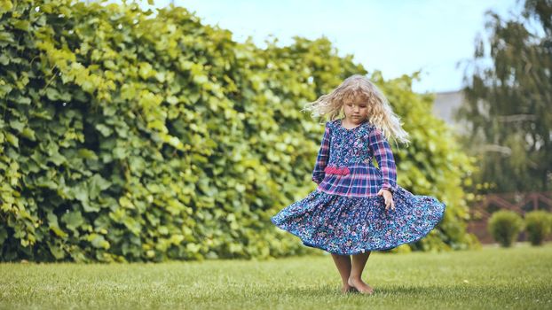 A little girl in a dress twirls in the garden