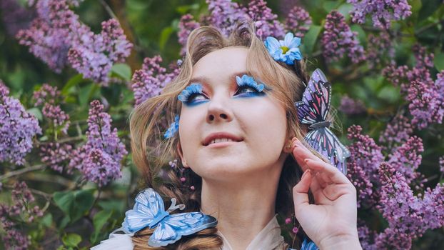 A young girl poses in lilac with a beautiful hairstyle of flowers and butterflies