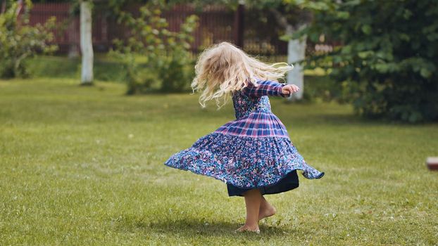 A little girl in a dress twirls in the garden