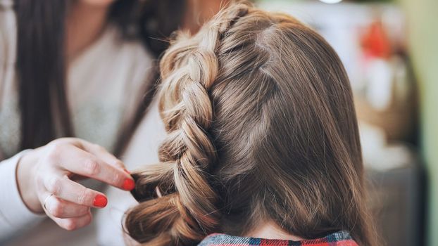 The girl makeup artist makes a braid for the model