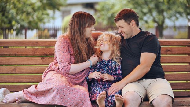 A young family on a swing in the garden. Parents kissing their daughter