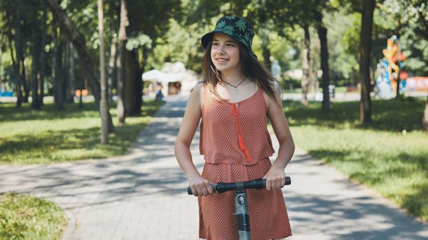 Portrait of a girl on an electric scooter riding in a park in the summer