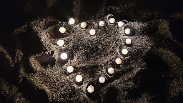 Heart made of small burning candles on sand in dark, concept of love and Valentine's Day