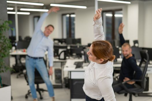 Three office workers warm up during a break. Employees do fitness exercises at the workplace