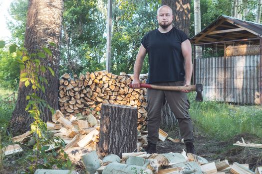 lumberjack stands with an ax near the chopped firewood , timber harvesting