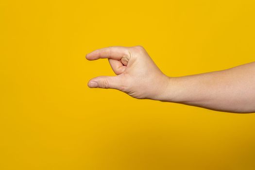 Sturdy man's hand making the small amount gesture isolated on yellow background