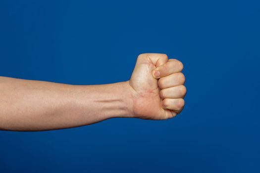 Robust man's hand isolated on a blue background showing a fist seen from the inside