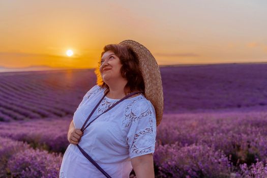 Woman lavender field sunset. Romantic woman walks through the lavender fields. illuminated by sunset sunlight. She is wearing a white blouse with a hat