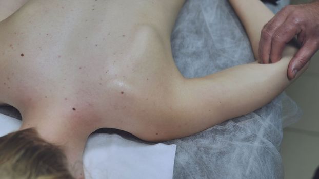 A masseur massages a girl's shoulder