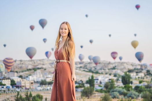 Tourist woman looking at hot air balloons in Cappadocia, Turkey. Happy Travel in Turkey concept. Woman on a mountain top enjoying wonderful view.
