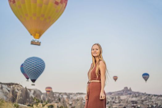 Tourist woman looking at hot air balloons in Cappadocia, Turkey. Happy Travel in Turkey concept. Woman on a mountain top enjoying wonderful view.