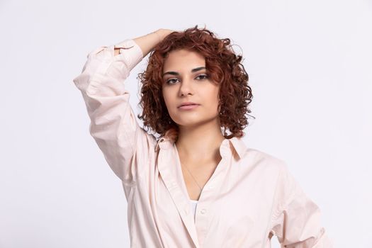 A young girl with short curly chestnut-colored hair. Hand carried up to head height. Light-colored long-sleeved blouse.