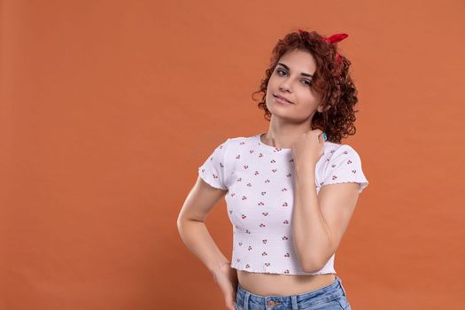 Beautiful girl stands and looks straight into the camera. Background in solid brick color. Curly hair in chestnut color.