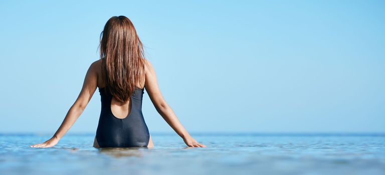 Back, young woman swimming at the beach on vacation in Mauritius and horizon of blue ocean water in summer. Calm female tourist in sea, freedom of travel lifestyle or relaxing on coastal destination.