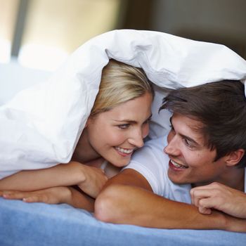 You, me and a blankie. a happy young couple enjoying a playful moment underneath the duvet