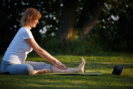 Step-by-step online yoga instructions. an attractive woman doing yoga at the park with her tablet beside her