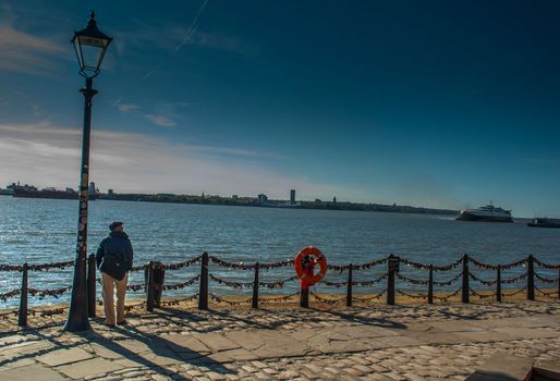 LIVERPOOL UK - May 13, 2019 - The young man stood alone under the Street lamp on the river walk in Royal Albert Dock, Liverpool