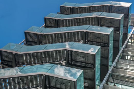 London 6 Jun 62 - Business building with metal emergency ladder / fire escape in modern office buildings with repeating structure and reflected sky and clouds.