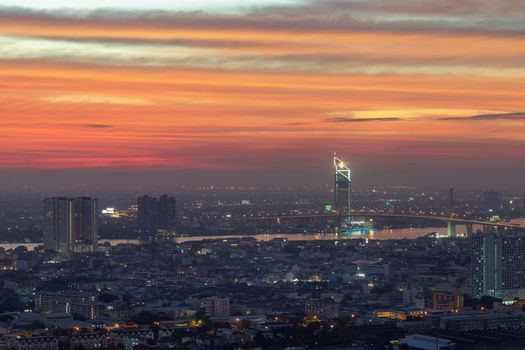 Bangkok, thailand - Dec 23, 2020 : Aerial view of Bangkok city Overlooking Skyscrapers and the Bridge crosses the Chao Phraya river with bright glowing lights at dusk. No focus, specifically.