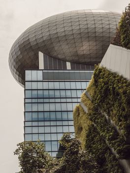 Bangkok, thailand - Mar 18, 2022 : Architectural View of Modern high rise building design of glass and concrete with Fern and green plants decorate on wall in front of. Selective focus.