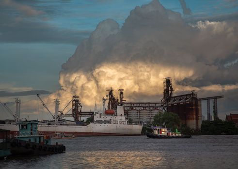 Bangkok, Thailand - 11 Jul 2021 : A cargo ship parked in front of Petroleum refinery on the Chao Phraya River in the evening. Selective focus.