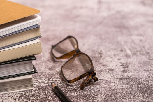 stack of old books with glasses and a black pencil with a blurred background