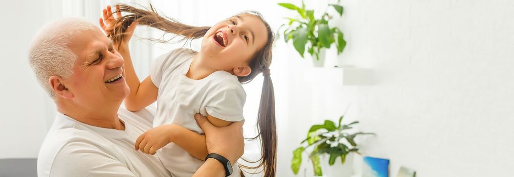 Middle-aged caucasian man playing with a little girl on the river bank. Man stands astoop ans holds his granddaughter on his back as she is "flying" Everybody's happy