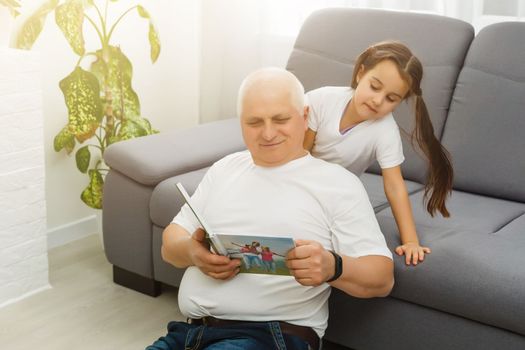 Happy little girl with grandfather watching photo books at home