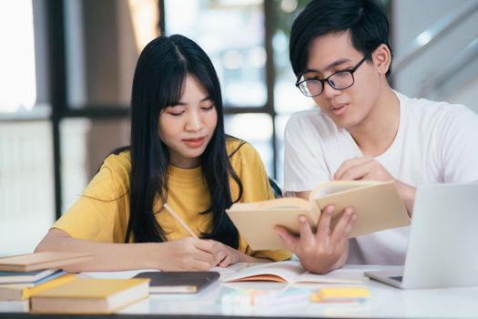 Young asian university students are studying for an exam. There are tutor books with friends. They are classmates that try to help each other. They have been tutoring for many hours in the campus.