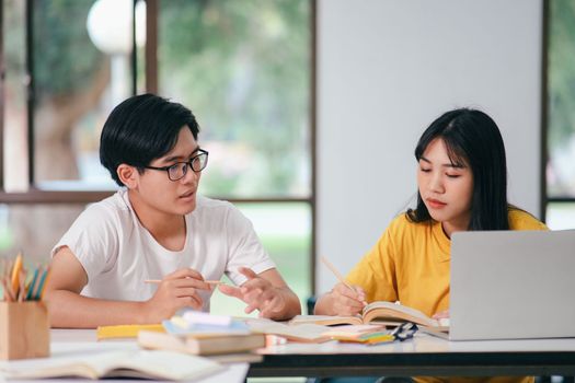 Young asian university students are studying for an exam. There are tutor books with friends. They are classmates that try to help each other. They have been tutoring for many hours in the campus.