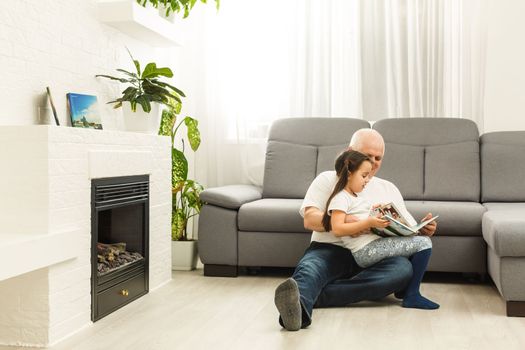 Happy little girl with grandfather reading story book at home