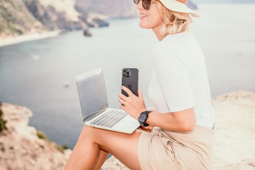 Digital nomad, Business woman working on laptop by the sea. Pretty lady typing on computer by the sea at sunset, makes a business transaction online from a distance. Freelance remote work on vacation