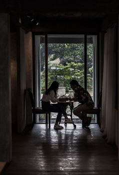 Chiang Mai,Thailand - Sep 07, 2020 : Shot of young adults sit and relaxing in a cafe and using mobile phone. Young man and woman at cozy coffee shop, Slow life concept. Dark tone, Focus and blur.