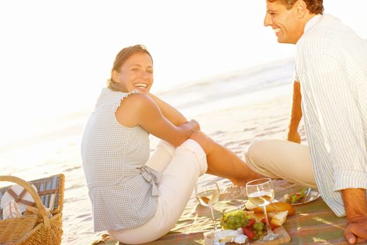 Sunset and romance on the beach. Rear view of a mature couple enjoying a picnic on the beach during sunset