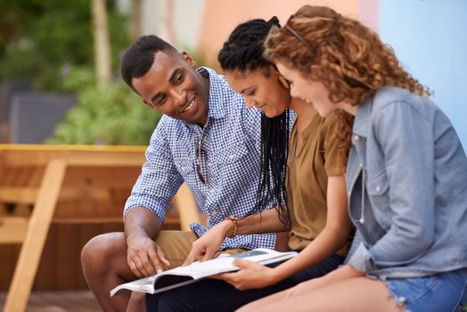 Magazines really help us unwind between classes. Three young friends sitting outdoors while on a break at campus