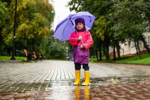 Child playing in autumn rain. Kid with umbrella. Outdoor fun for kids by any weather. Rain waterproof wear, boots and jacket for children.