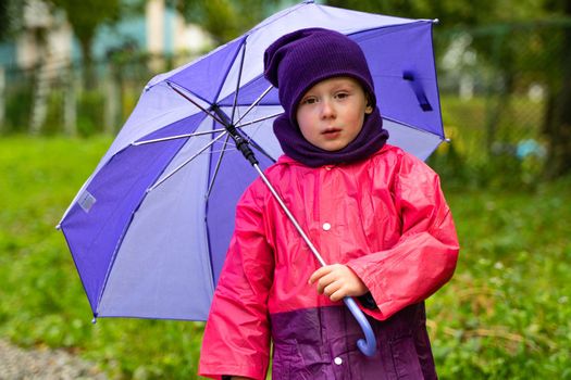 Child with an umbrella walks in the rain. Little boy with umbrella outdoors.