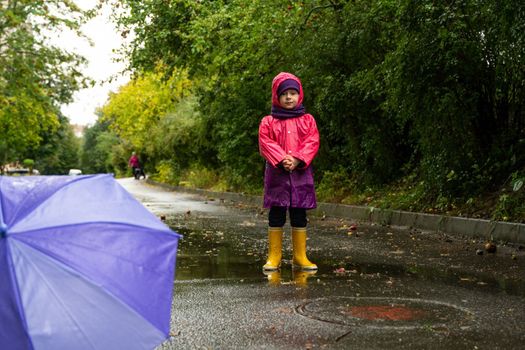 Child playing in autumn rain. Kid with umbrella. Outdoor fun for kids by any weather. Rain waterproof wear, boots and jacket for children.