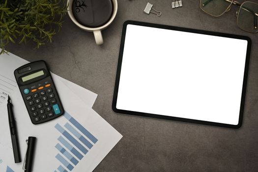 Tablet with empty display, calculator, financial reports and supplies on black slate texture background.