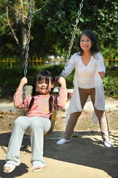 Joyful little girl having fun on swing with grandmother, spending weekend time together. Generational, family and love concept.